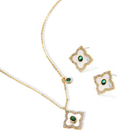 Gold-plated quatrefoil pendant and earrings with white enamel, emerald CZ center stones, and crystal borders on white background.