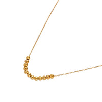 Delicate gold-plated necklace with graduated spherical beads forming gentle smile curve on beige background