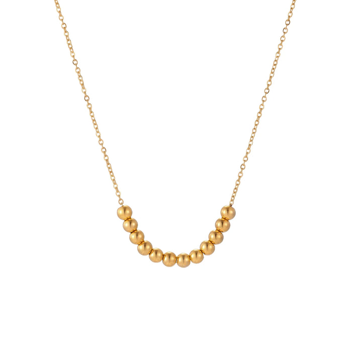 Delicate gold-plated necklace with graduated spherical beads forming gentle smile curve on beige background