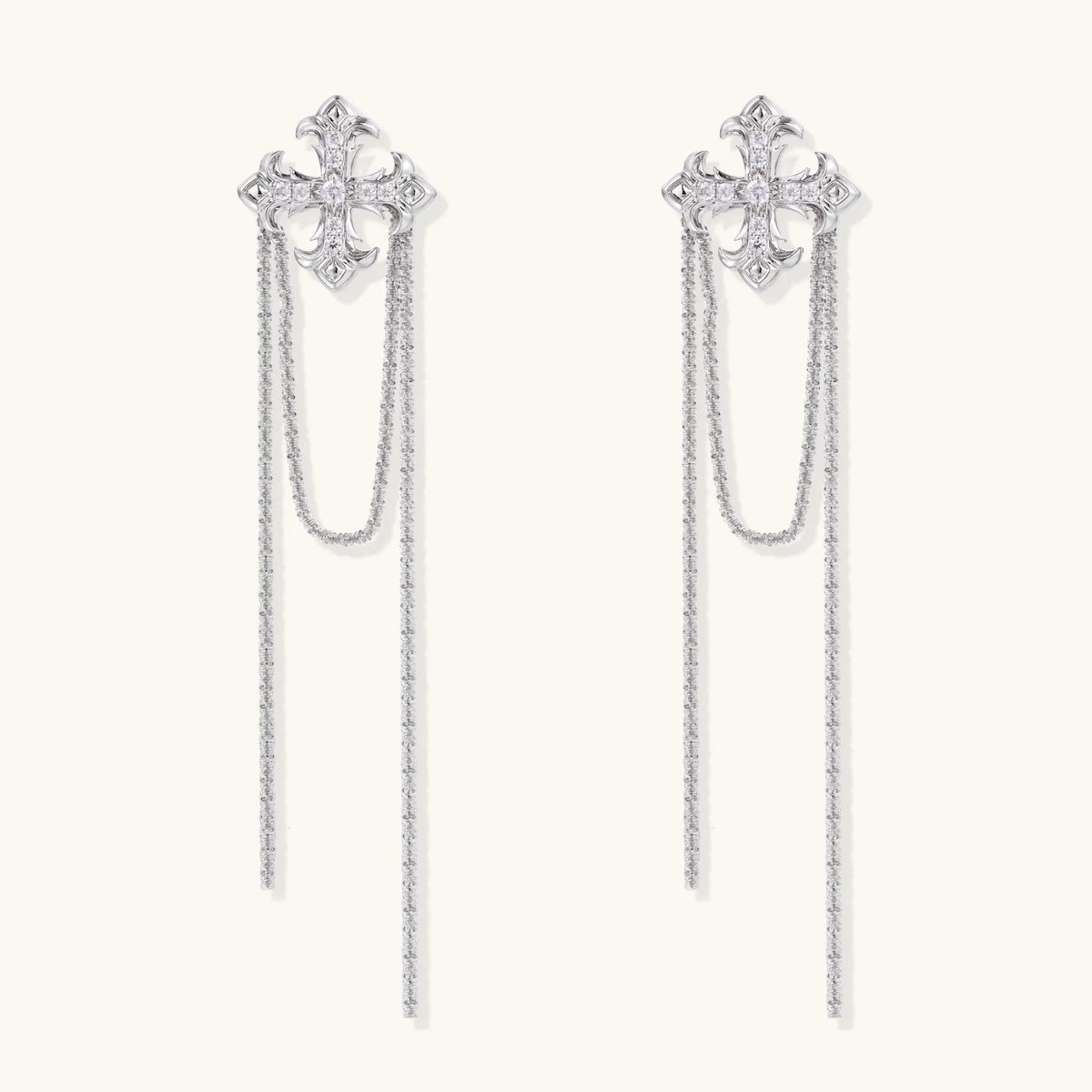 White gold plated baroque cross stud earrings with long cascading zirconia chains on cream background