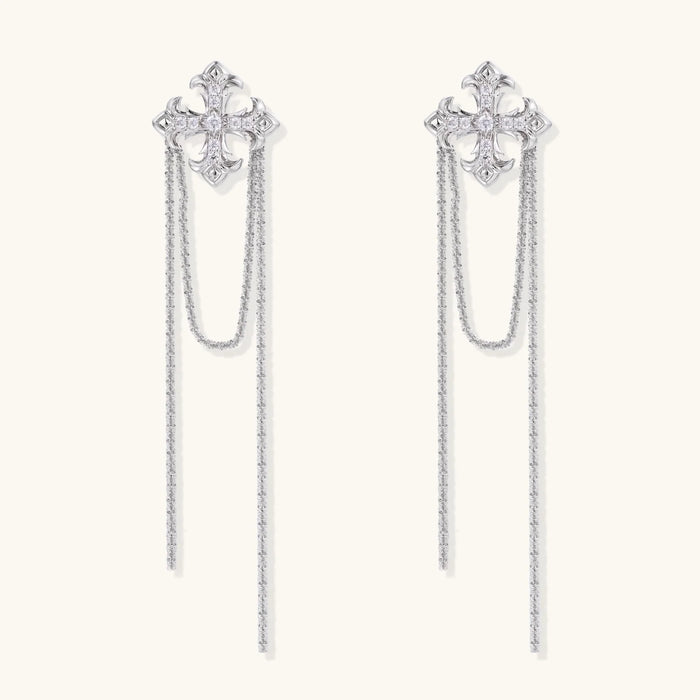 White gold plated baroque cross stud earrings with long cascading zirconia chains on cream background