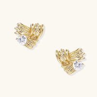 Pair of sculptural gold-plated wing stud earrings with zirconia stones on cream background, showing dimensional feather design