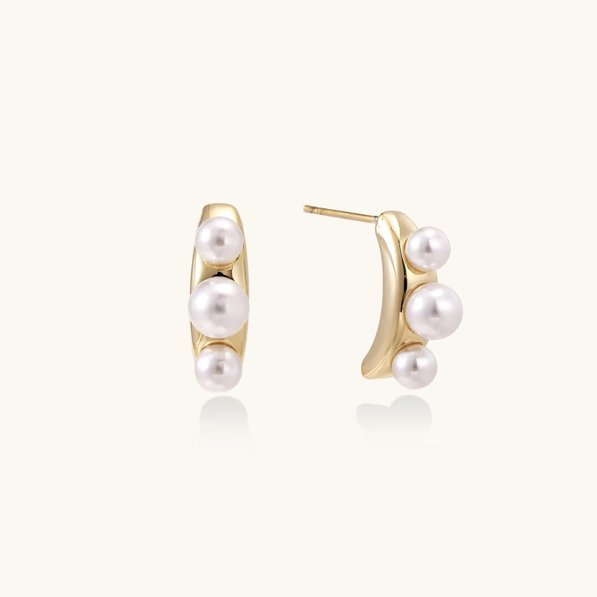 14K gold-plated curved stud earrings with three white freshwater pearls aligned vertically on cream background