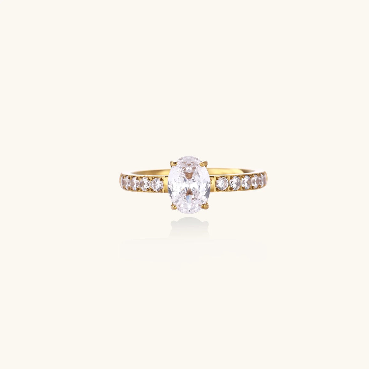 Gold-plated solitaire ring with oval zirconia center stone and pavé band on cream background