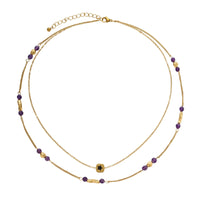 Two layered gold-tone necklaces with purple stone beads and star pendant against cream background.