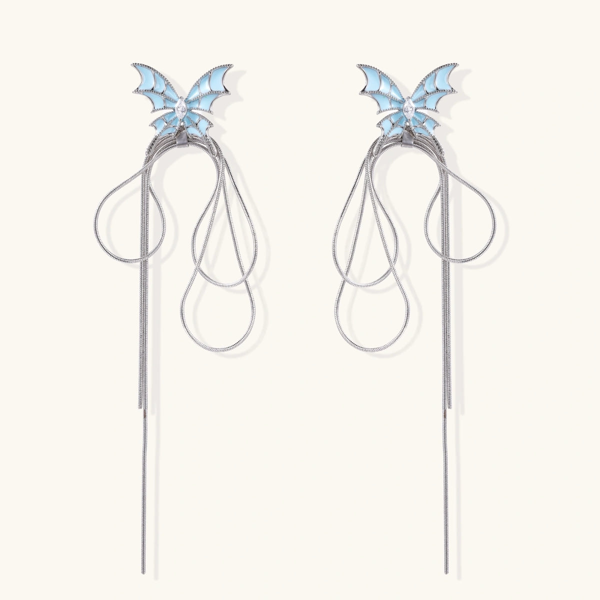 Long silver-tone earrings with powder blue enamel butterfly studs and flowing chain tassels on cream background