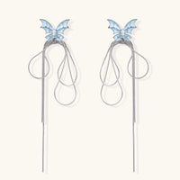 Long silver-tone earrings with powder blue enamel butterfly studs and flowing chain tassels on cream background