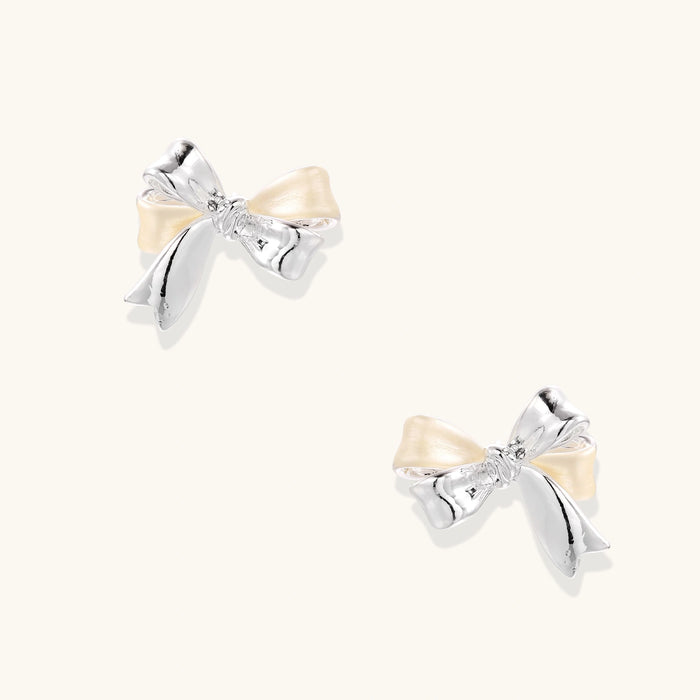 Dimensional bow stud earrings in white gold plated brass with silver and cream two-tone finish on neutral background