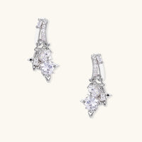 White gold-plated huggie earrings with geometric emerald-cut zirconia clusters in starburst formation on beige background