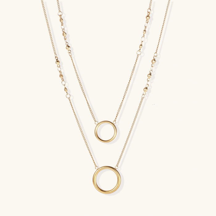 Layered gold necklace set with two open circle pendants and mixed chain styles on beige background