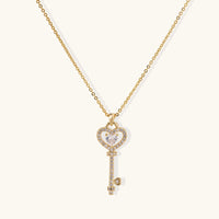 Delicate gold key pendant with heart-shaped bow and crystal pavé detailing on fine chain against cream background.