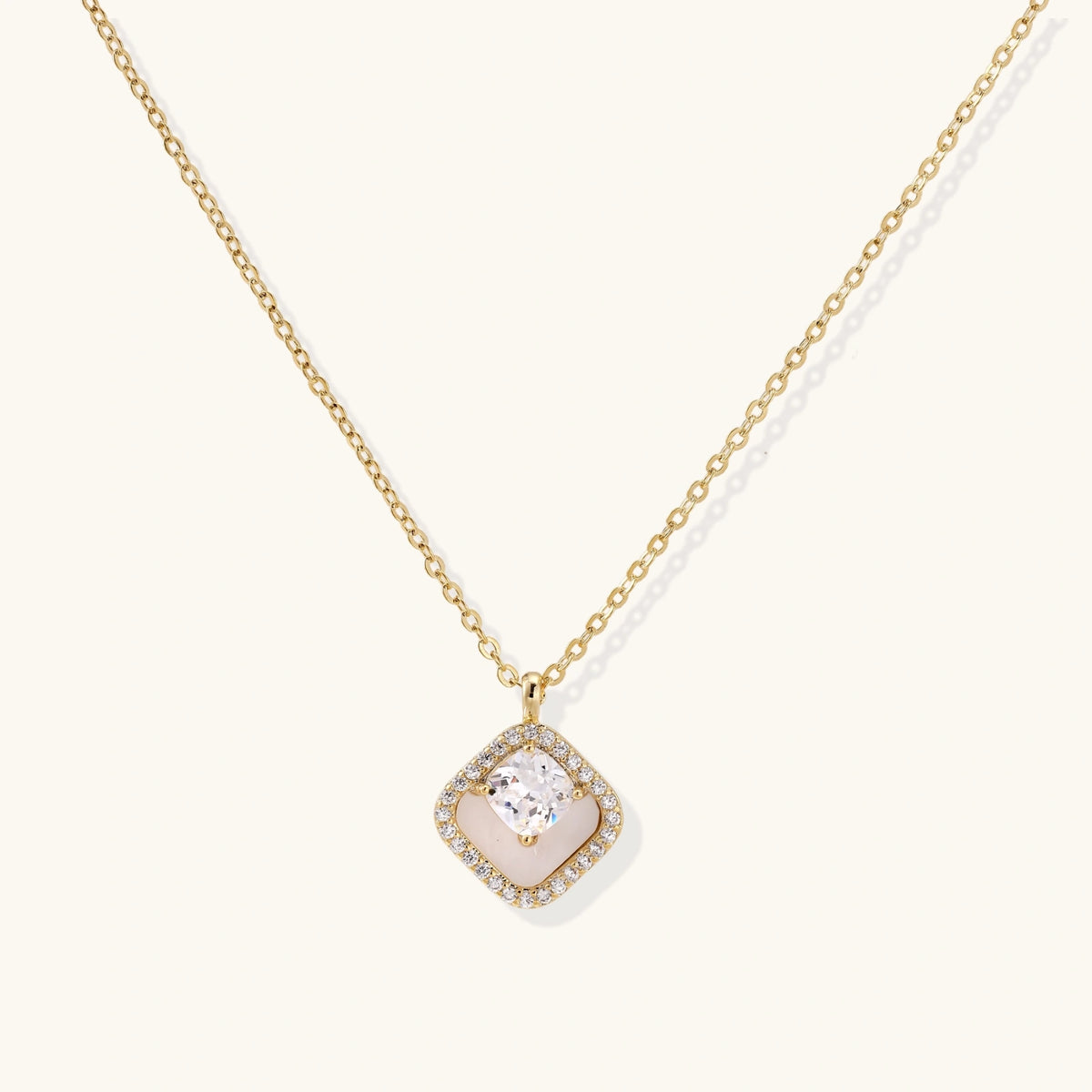 Gold quatrefoil pendant with crystal center on iridescent mother-of-pearl base, adjustable gold chain on cream background