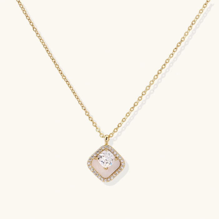 Gold quatrefoil pendant with crystal center on iridescent mother-of-pearl base, adjustable gold chain on cream background