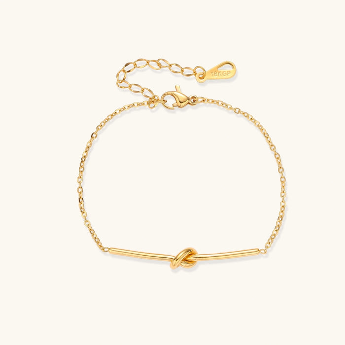 Delicate gold chain bracelet with minimalist bar and centered knot detail on cream background