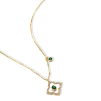 Gold-plated quatrefoil pendant and earrings with white enamel, emerald CZ center stones, and crystal borders on white background.